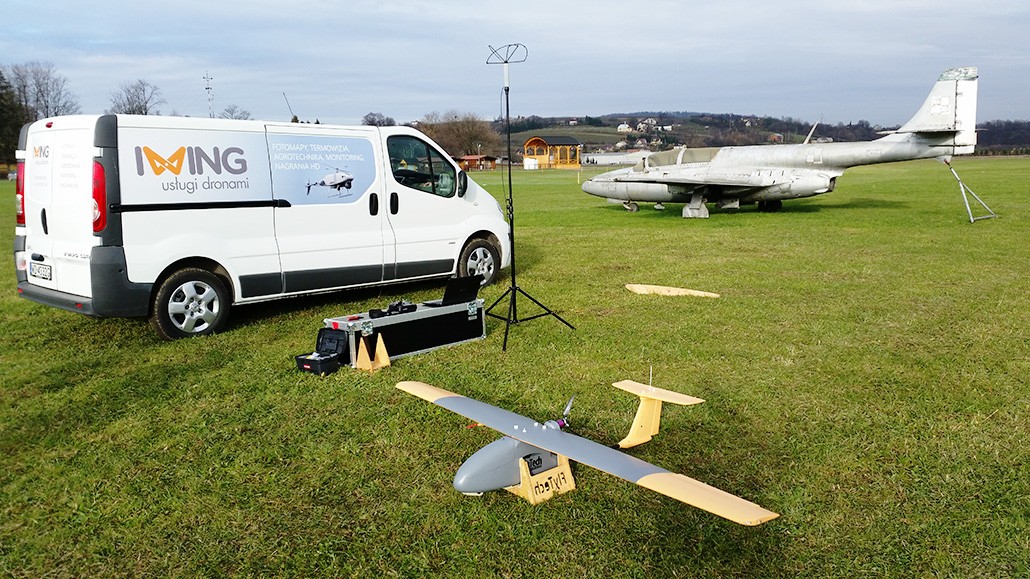 dron i oprzyrządowanie stoją obok samochodu dostawczego na zielonej trawie