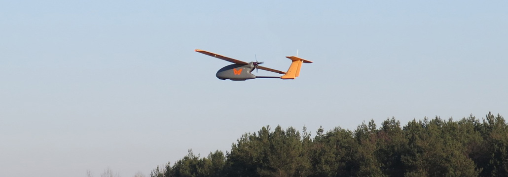 dron płatowiec lecący nad lasem na tle nieba